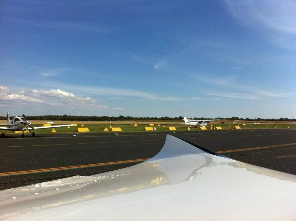 Looking over VH-EZT's wing across the parking area at Jandakot