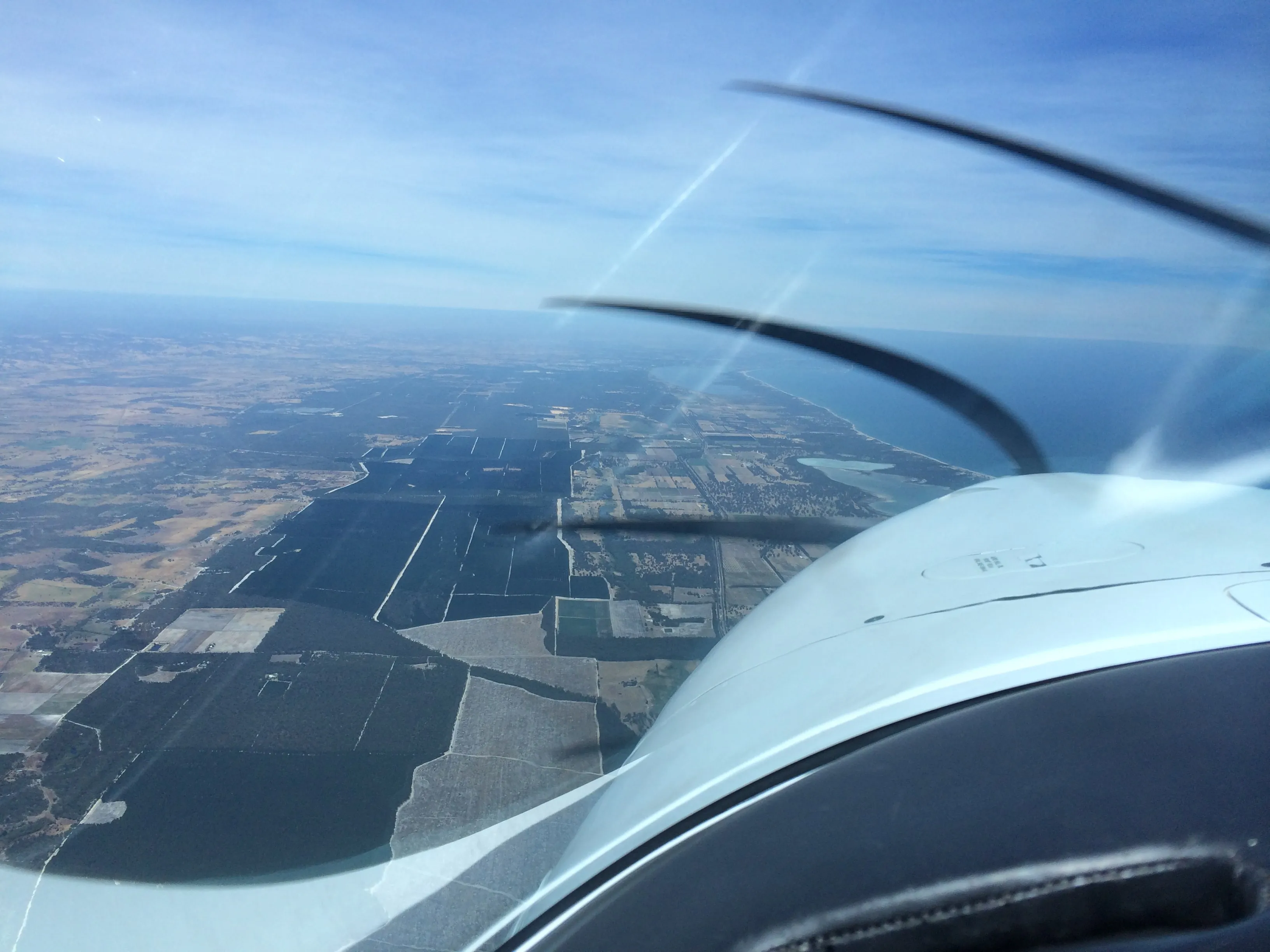 Farmland and tree plantations near the coast seen over VH-EZT's nose